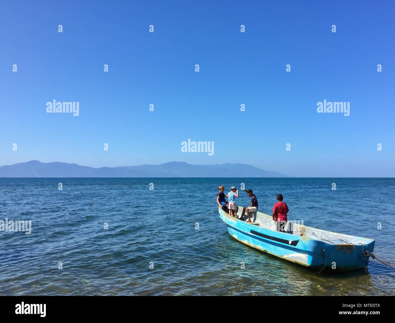 Kinder spielen und Angeln auf einem alten Boot auf das Meer mit Bergen im Hintergrund in Honduras Stockfoto