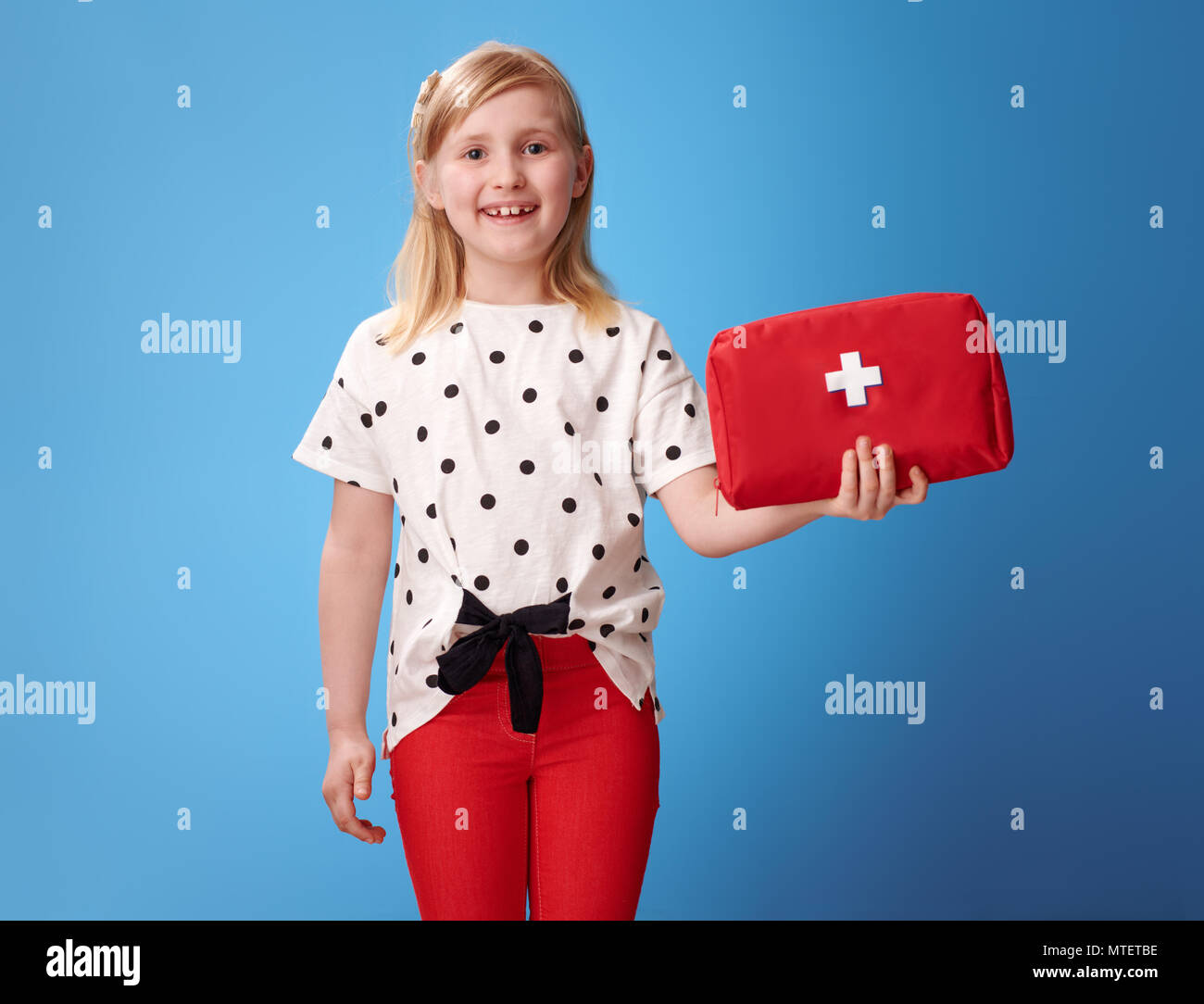 Lächelnde Mädchen in roten Hosen anzeigen Erste Hilfe Kit isoliert auf Blau Stockfoto