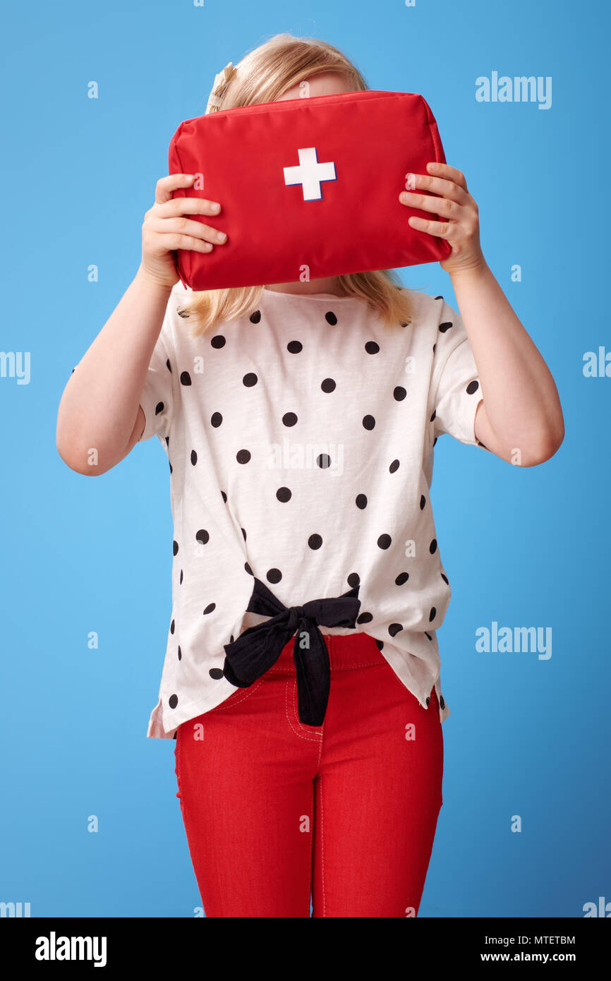 Moderne Kind in roten Hosen halten Erste Hilfe Kit im Gesicht auf blauem Hintergrund isoliert Stockfoto