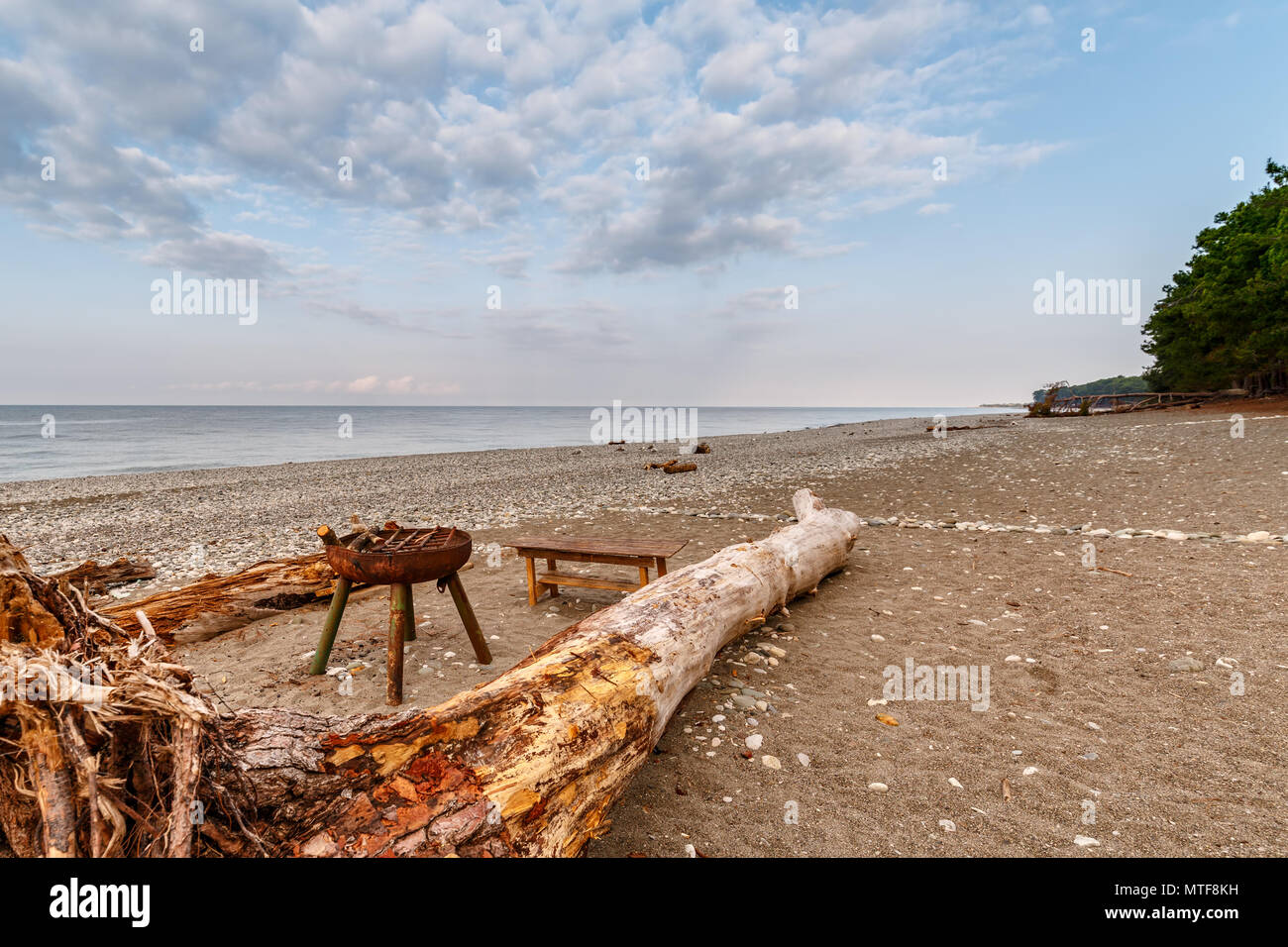 Metall Brazier, den Kofferraum eines gefallenen Baum und eine Bank befinden, stellen Sie sich auf die einsame Ufer eines ruhigen Meer an einem sommerlichen Abend Stockfoto