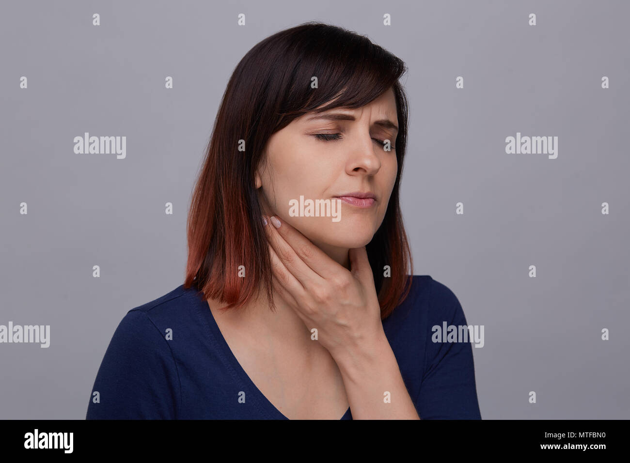 Closeup Porträt der jungen Frau auf grauem Hintergrund leidet an einer Halsentzündung, Holding finger Mandeln und schließen die Augen vor Schmerz. Stockfoto