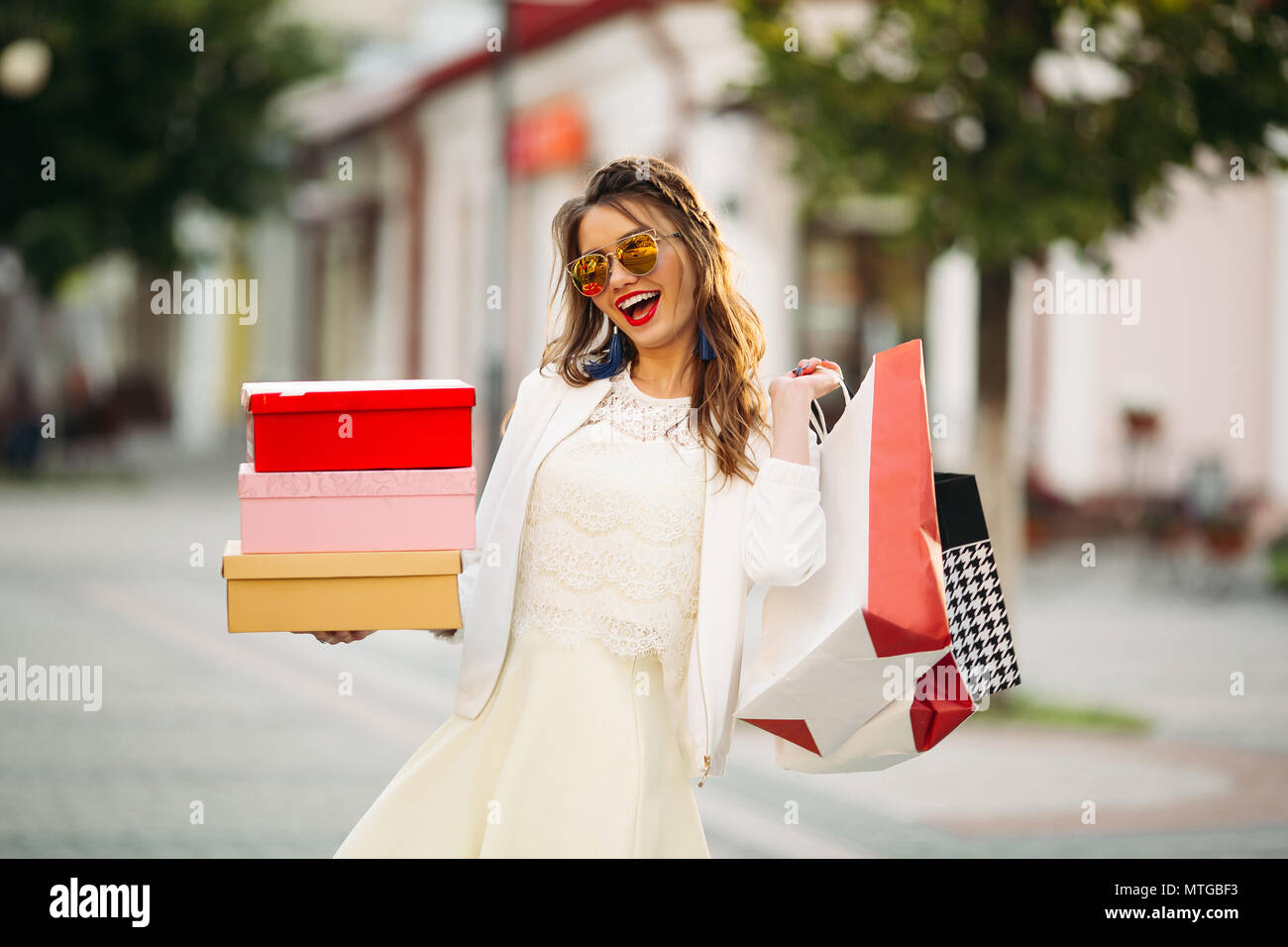 Trendige Mädchen in der Sonnenbrille mit Schuhkartons und Einkaufstaschen in t Stockfoto