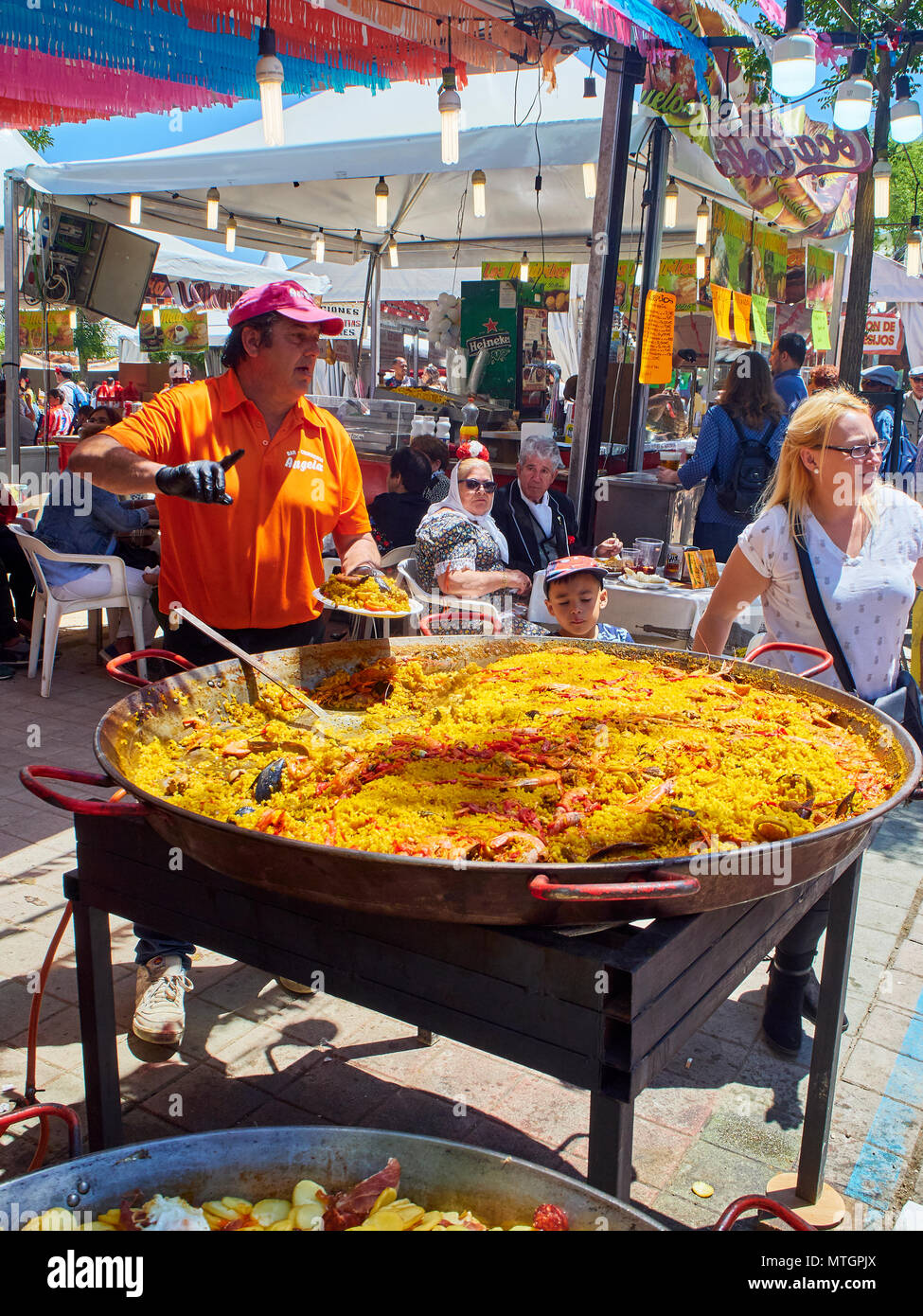 Madrid, Spanien - 15. Mai 2018. Ein Koch serviert spanische Paella in einem Stall in eine Gastronomische Messe unter dem wachsamen Auge eines asiatischen Jungen. Stockfoto