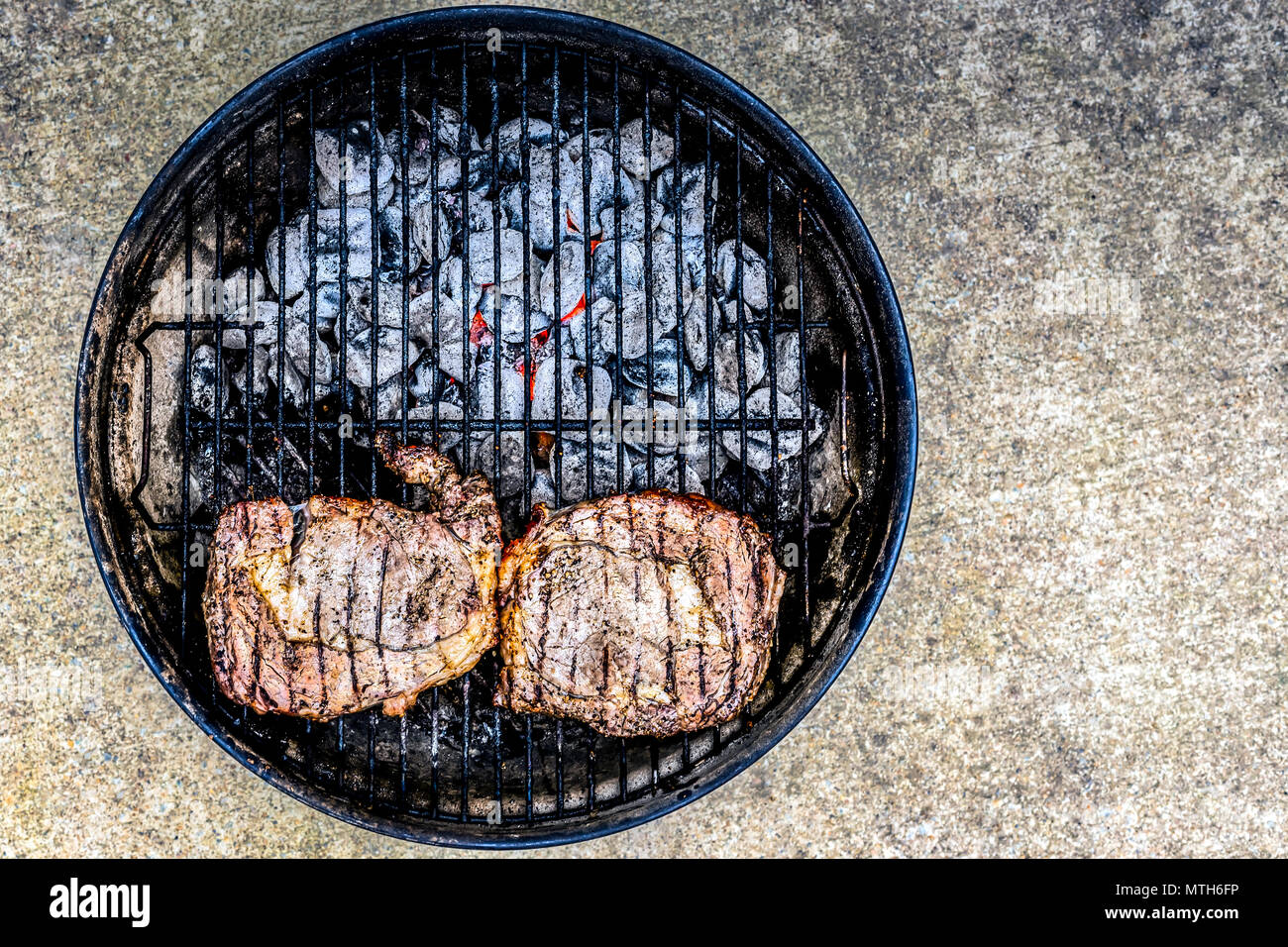 Zwei erfahrene Steaks über Kohlen sitzen auf einem kleinen Grill im Freien. Stockfoto