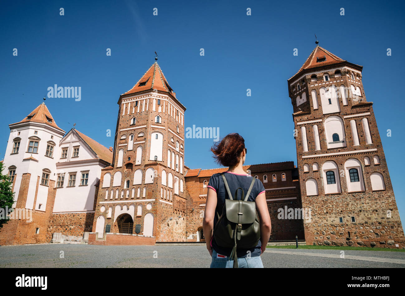 Junge Frau Reisenden mit Rucksack schaut auf mittelalterliche Burg in Mir, Weißrussland Stockfoto