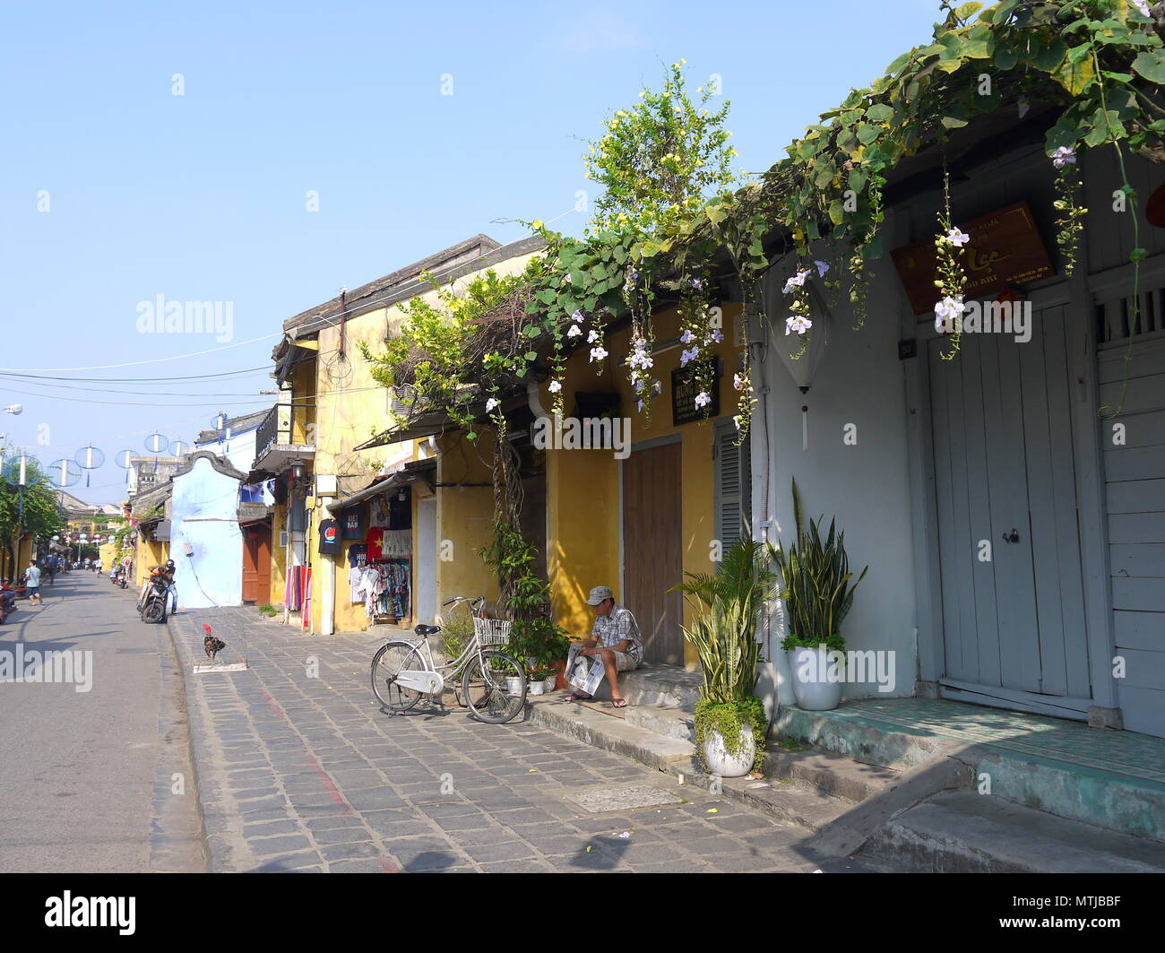 HOI AN, VIETNAM - 17. MÄRZ 2018: ein Mann sitzt auf einem Schritt vor einem closed shop lesen Zeitung frühe sonniger Morgen in Hoi An Stockfoto