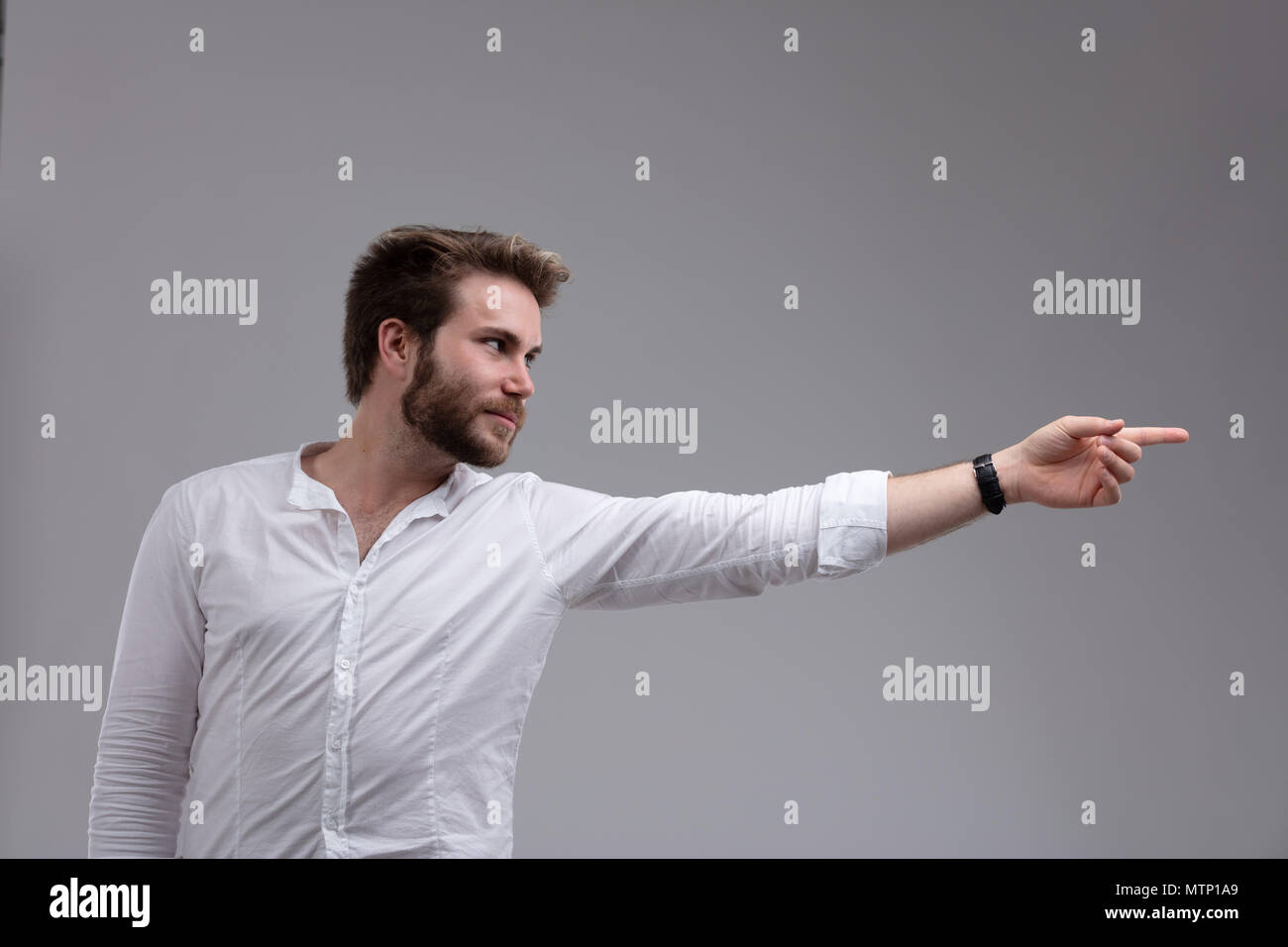 Attraktive bärtiger Mann, der auf der Seite mit gestrecktem Arm isoliert auf Grau mit Kopie Raum Stockfoto