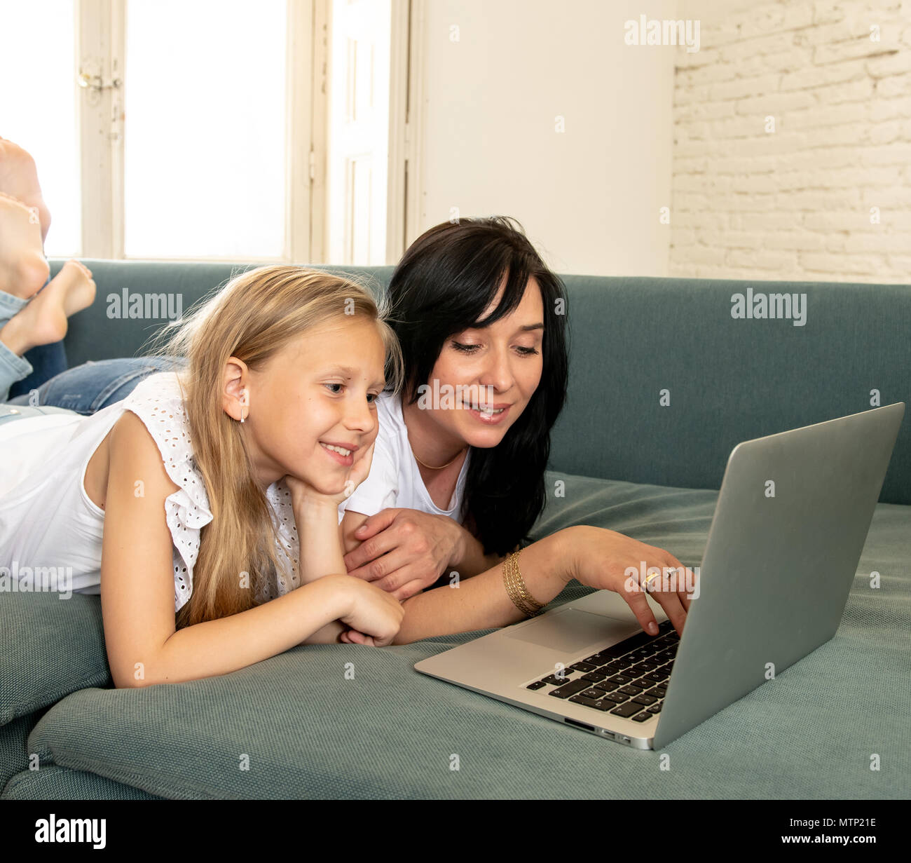 Schöne blonde süsse kleine Mädchen und Mama spielen zusammen lächeln und in Verbindung mit einem Laptop auf der Couch zu Hause. Happy Family, digital Stockfoto