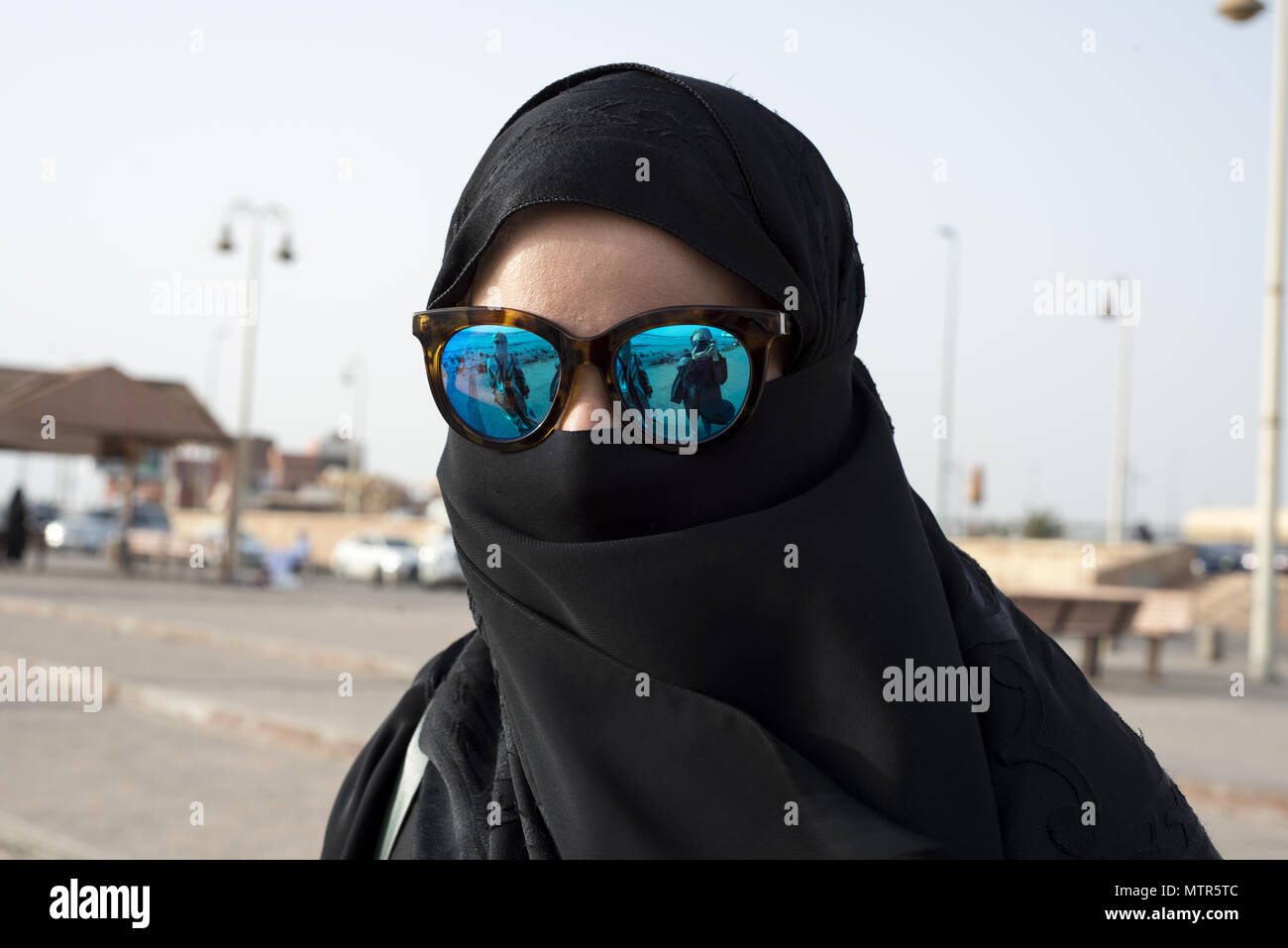Eine saudische Frau trägt einen schwarzen Abaya und Hijab schützt die Augen vor der Sonne mit blau Sonnenbrille Stockfoto