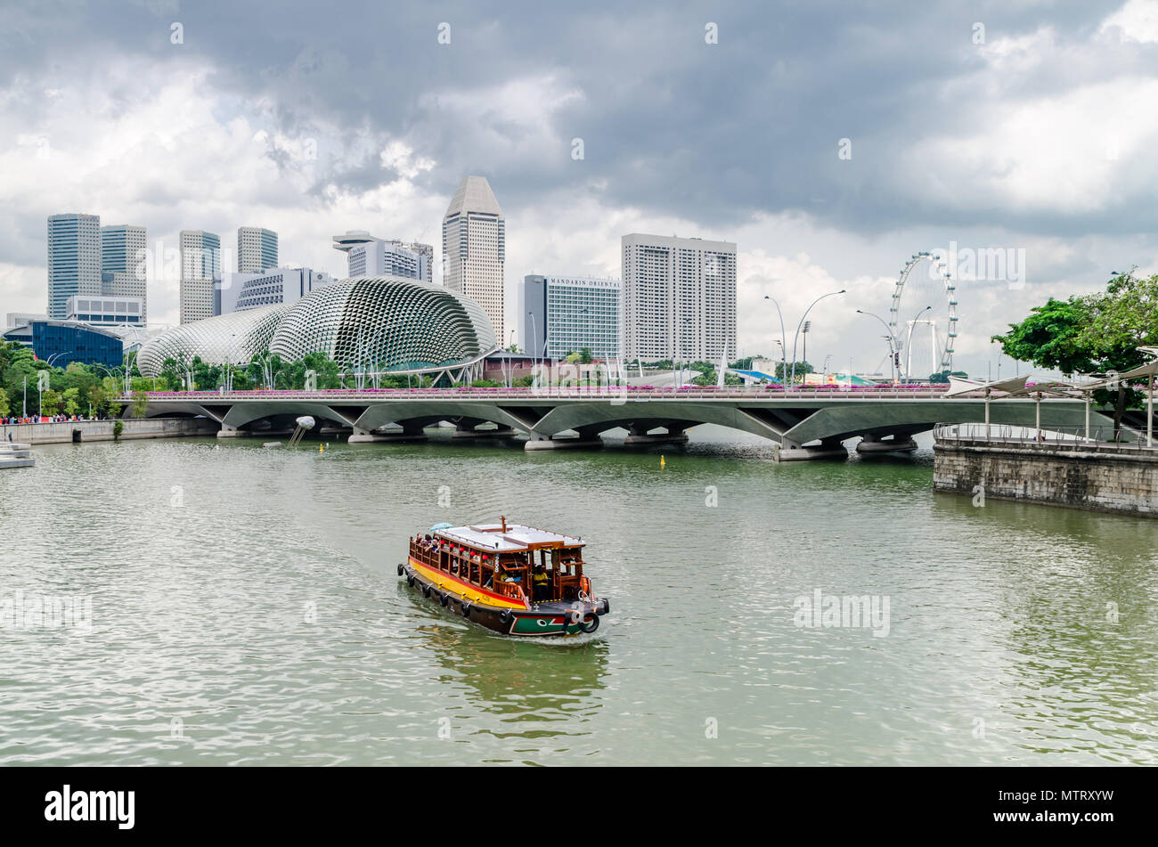 Eine Kreuzfahrt Boot wie die twakows Fahrt durch die berühmten Singapore River bekannt. Das Gebäude an der Rückseite ist die berüchtigte Theater an der Bucht, Esplanade. Stockfoto