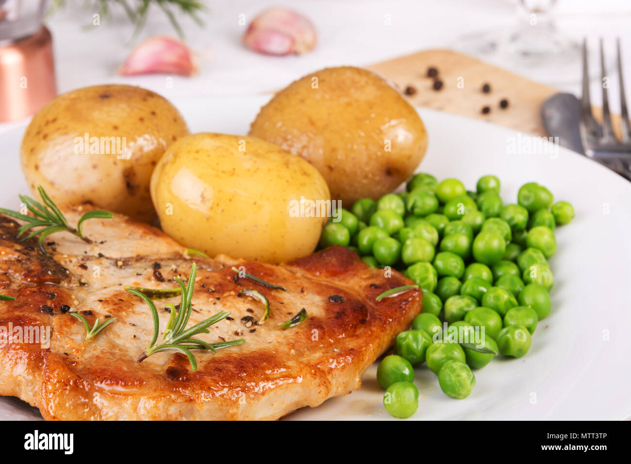 Nahaufnahme von Schweinekotelett, gekochte Kartoffeln und grünen Erbsen auf einem Teller serviert. selektive Fokus Stockfoto