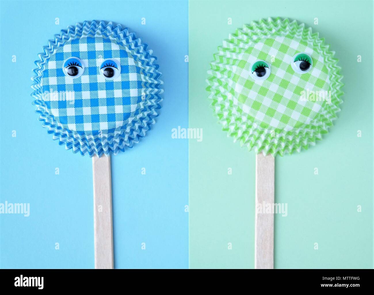 Zwei cupcake Formen aus Papier mit wackligen Augen, Eis Popsicle Sticks, einfaches Konzept in pastelligen Farben Grün und Blau. Lustige kreative Bild- und Text- raum Stockfoto