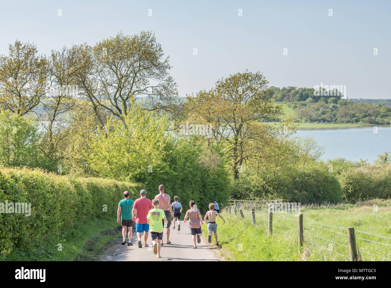 Eine Gruppe von drei Männern zu Fuß eine Straße an einem heißen Tag zu Rutland Water Lake, England, als vier Kinder laufen an ihnen vorbei. Stockfoto