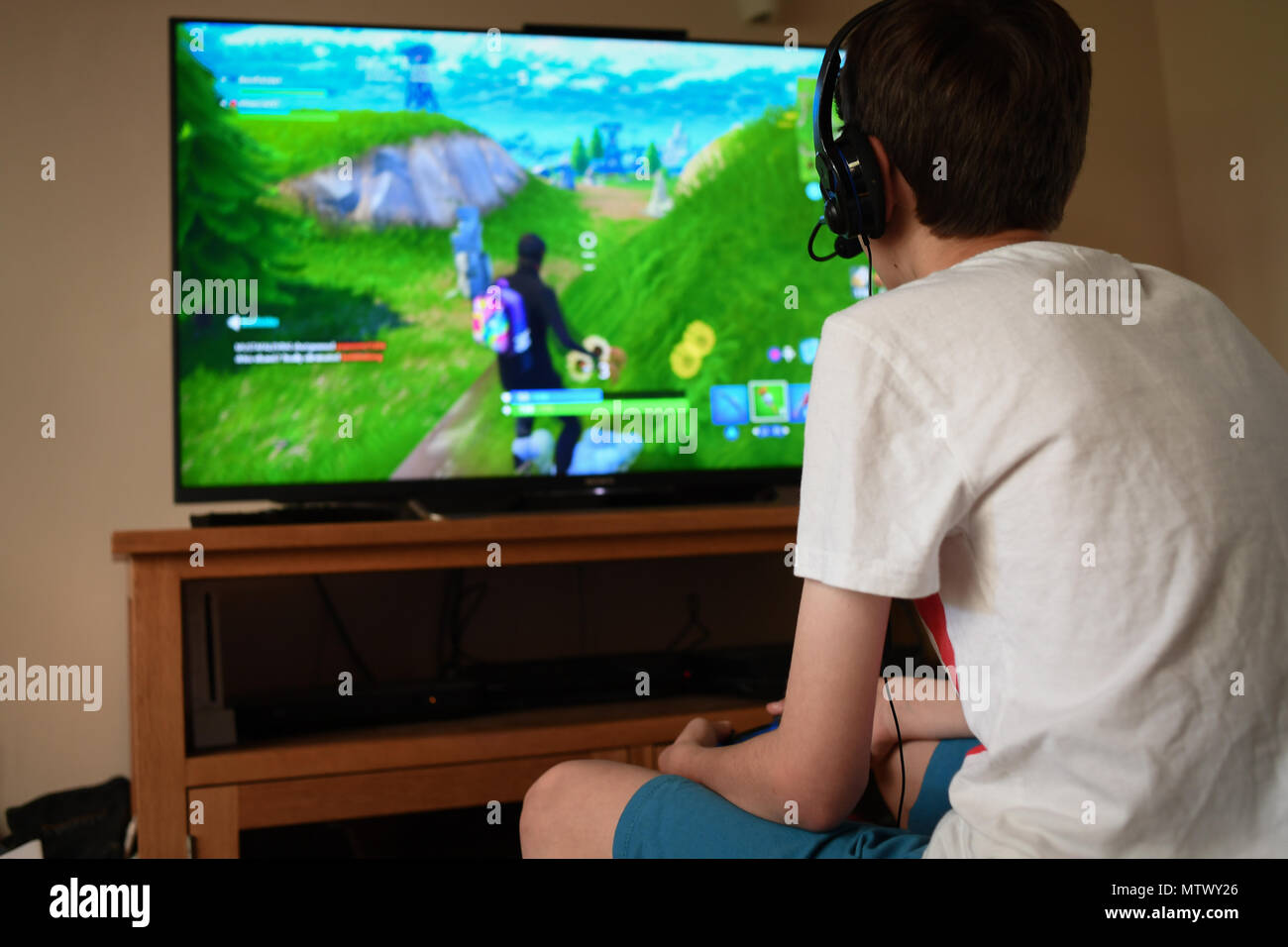 Ein Teenager Alter 13 spielt Fortnite computer spiel auf der PS4 über ein Headset mit anderen Spielern in seine Gruppe zu kommunizieren. Stockfoto