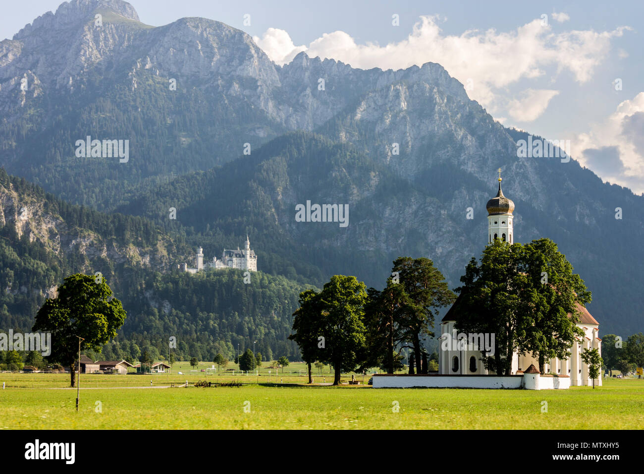 Schwangau, Deutschland. Malerische long shot Blick auf St. Coloman Kirche, mit dem weltberühmten Schloss Neuschwanstein im Hintergrund das Schloss Stockfoto