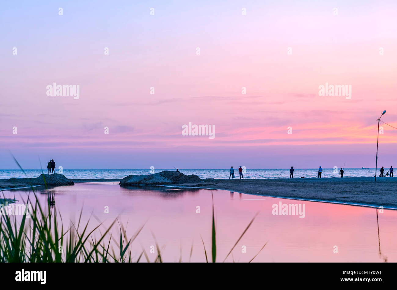 Touristen und Fischer sind am Schwarzen Meer und genießen Sie den schönen Sonnenuntergang. Ein Paar in Liebe nimmt eine selfie gegen den Sonnenuntergang. Stockfoto