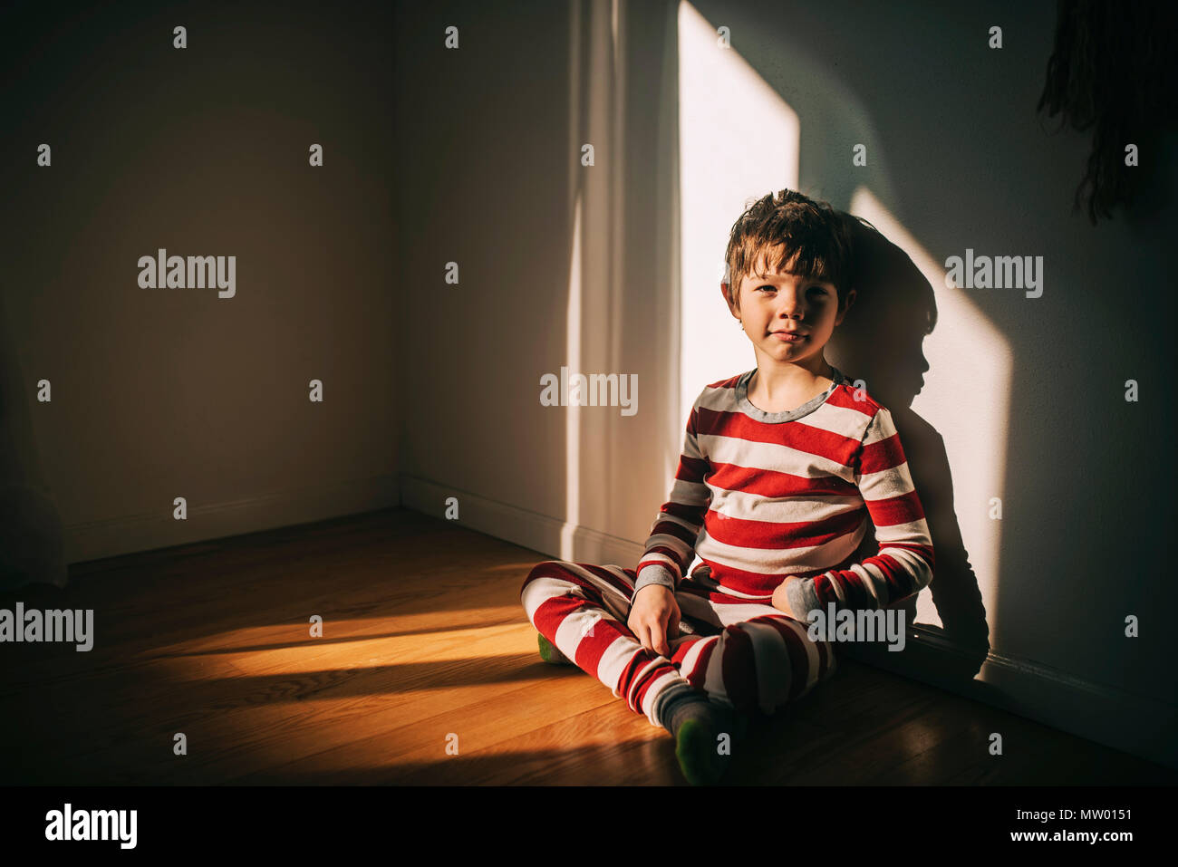 Junge sitzt auf dem Boden lehnte sich gegen eine Wand. Stockfoto