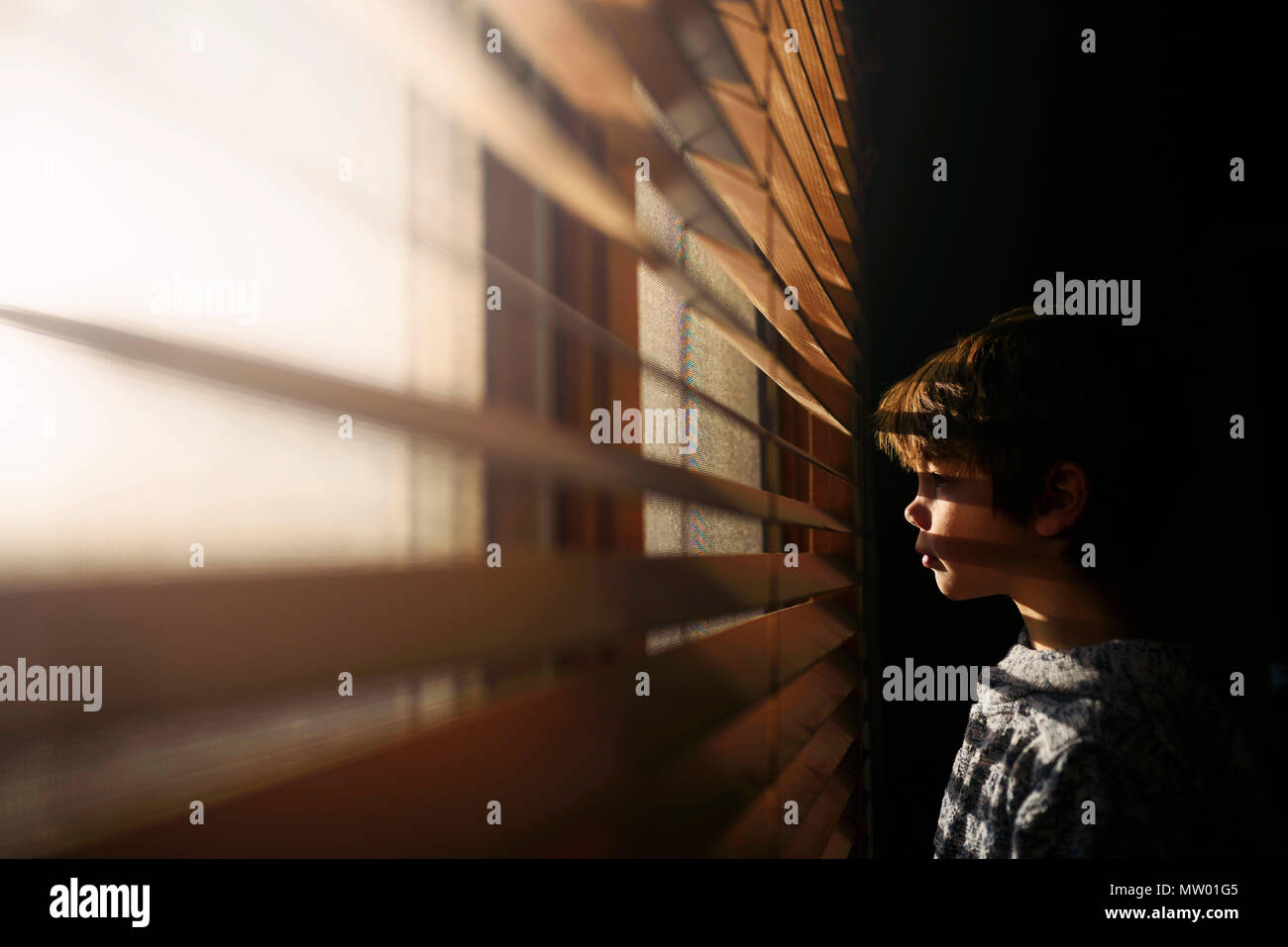 Junge durch ein Fenster schauen durch Jalousien Stockfoto