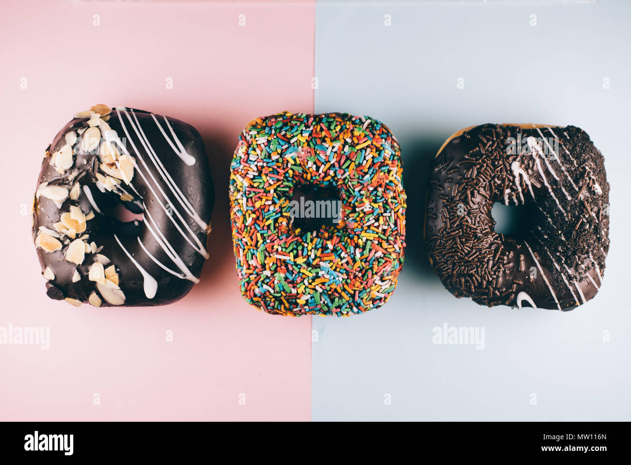 Drei quadratische Form Donut mit verschiedenen Toppings auf Blau und Rosa Hintergrund. süße Speisen und ungesundes Essen Konzept Stockfoto