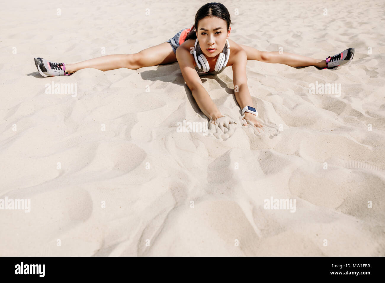 Asiatische Sportlerin mit Kopfhörern tun Split auf Sand Stockfoto