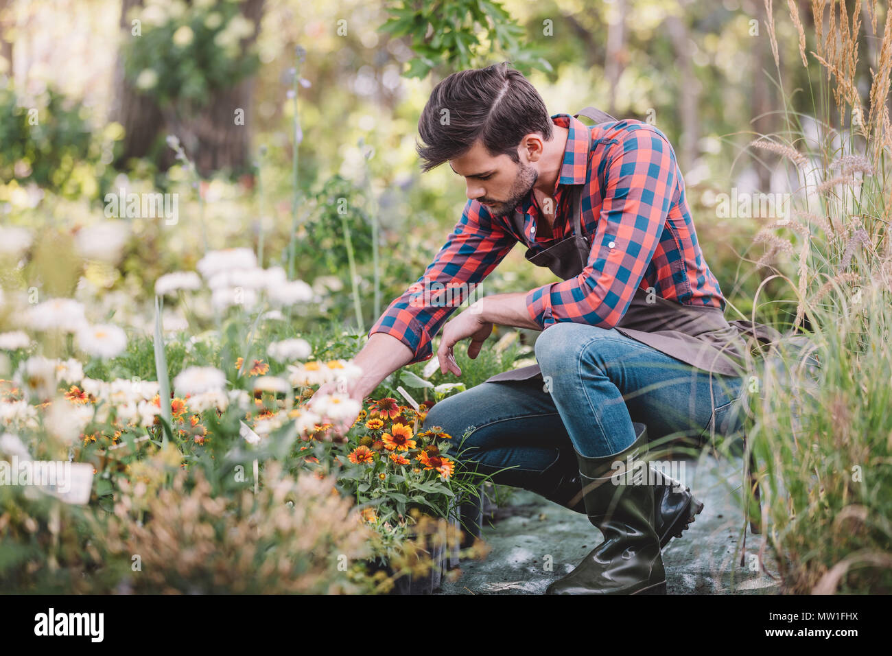 Junge Gärtner in Schürze und Gummistiefel Kontrolle Blume im Garten
