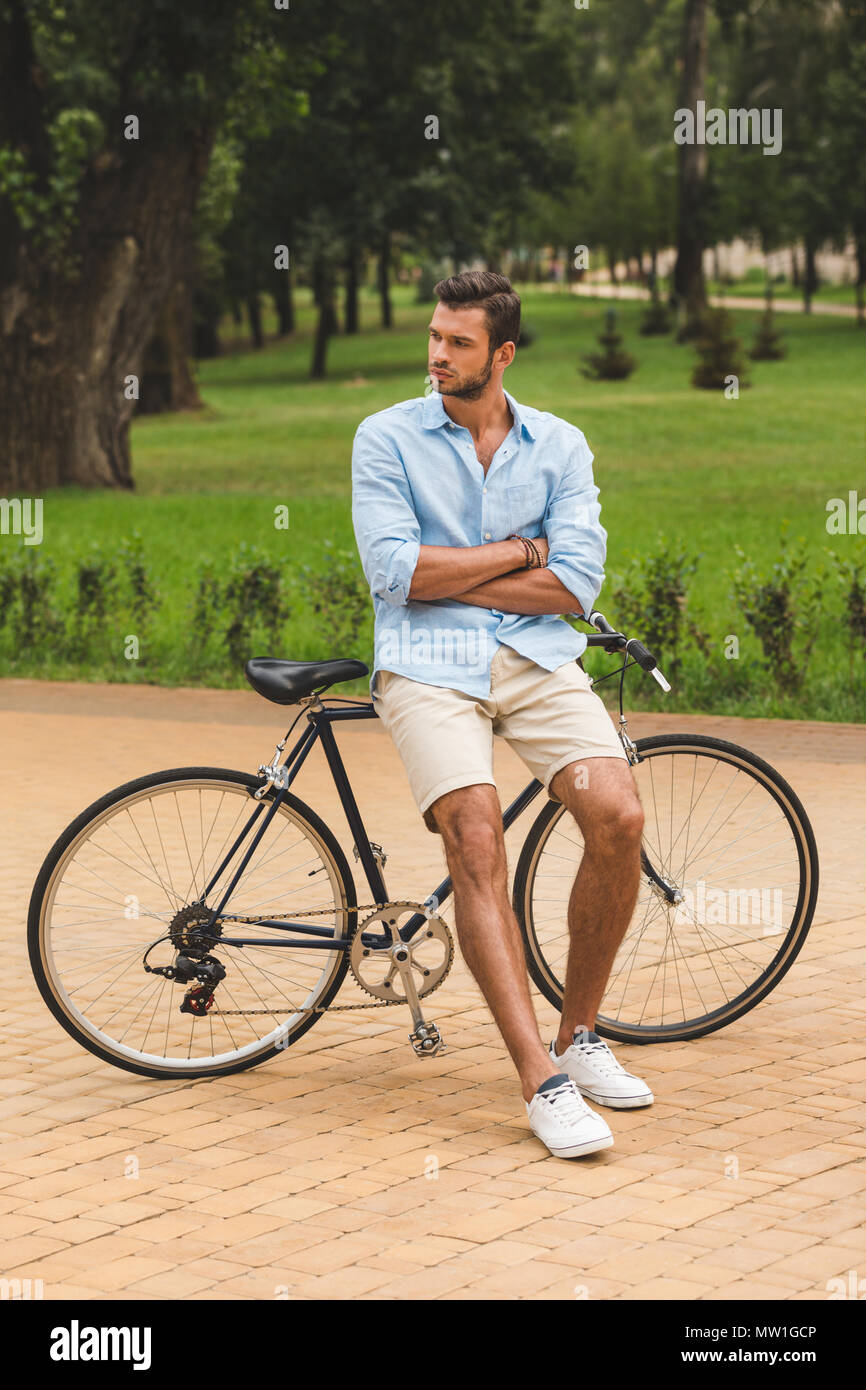 Nachdenklicher Mann mit verschränkten Armen lehnte sich auf dem Fahrrad und Wegsehen in Park Stockfoto