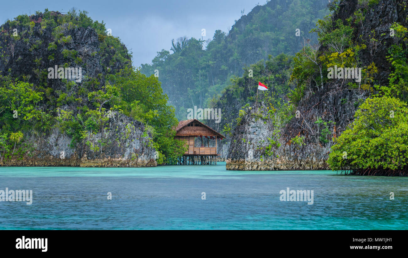 Bambushütte zwischen einigen Felsen unter Regen in der Bucht mit indonesischen Flagge, Pianemo Inseln, Raja Ampat, West Papua, Indonesien Stockfoto