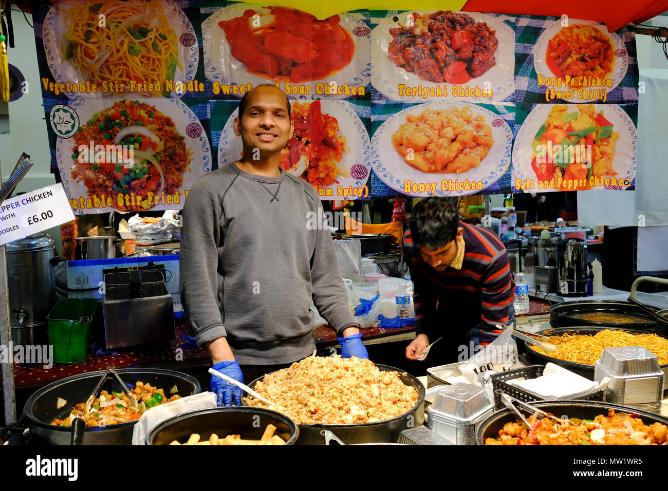 Lächelnd Anbieter verkaufen verschiedene Gerichte im Fast food in Brick Lane Market, London, England, UK. Stockfoto