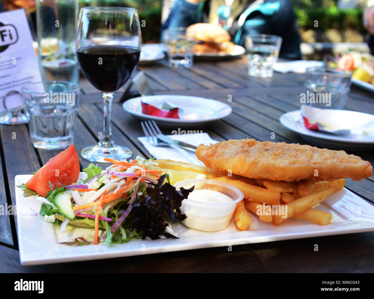 Ein barramundi Fish und Chips Schüssel serviert mit Salat und einem Glas Rotwein. Stockfoto