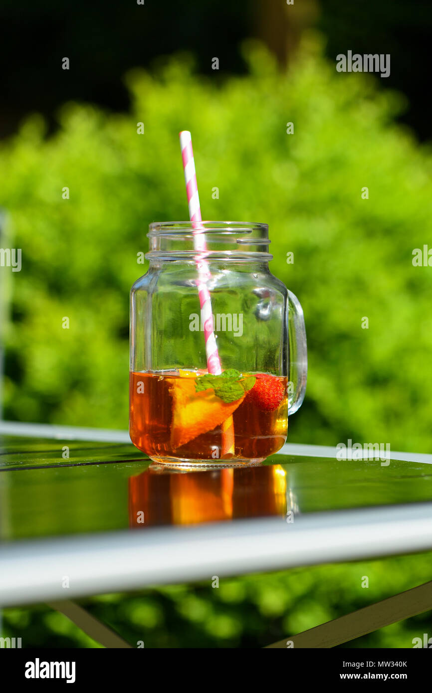 Ein Glas pimms in einem Marmeladenglas Glas mit einem Papier Stroh außerhalb an einem Sommertag. Stockfoto