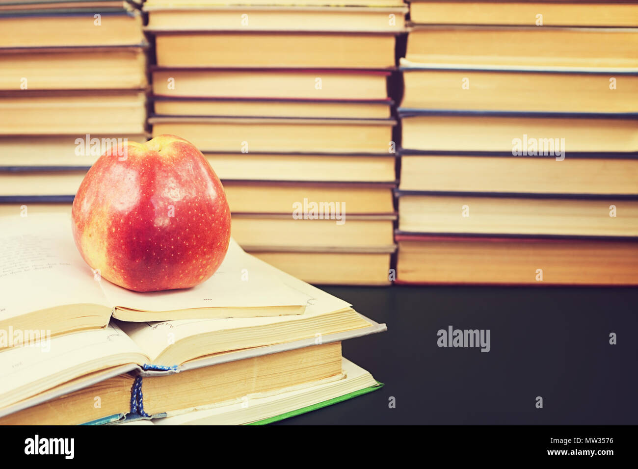 Roter Apfel auf dem offenen Buch gegen die Bücher Hintergrund Stockfoto