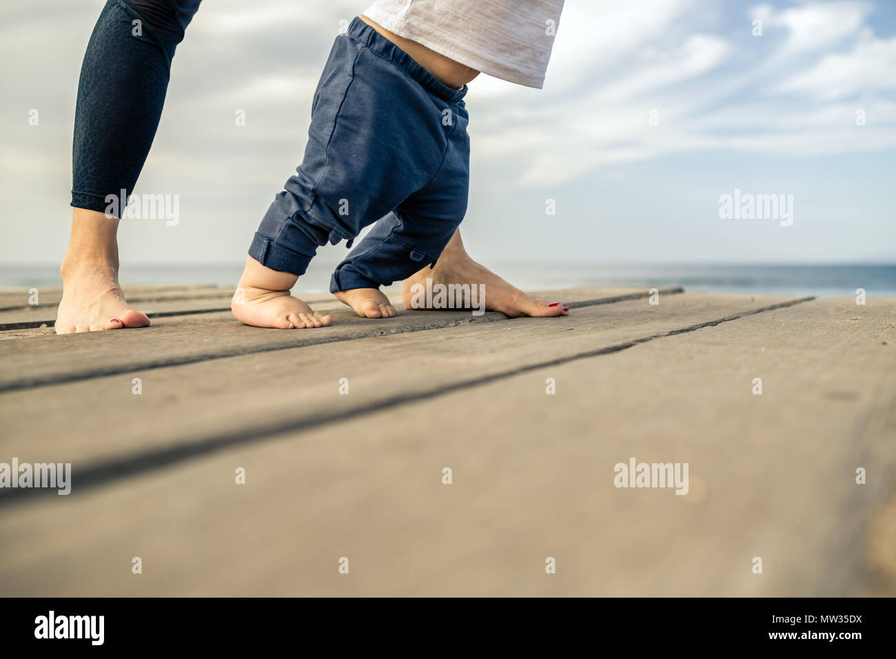 Baby Boy Walking am Strand in einer wunderschönen Sommertag. Mutter mit Sohn laufen lernen, erste kleine kleinkind Schritte. Stockfoto