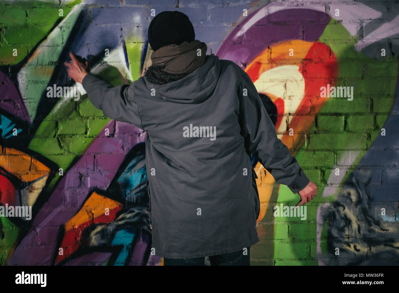 Rückansicht des Menschen malen Graffiti mit Aerosol Farbe auf Wand bei Nacht Stockfoto