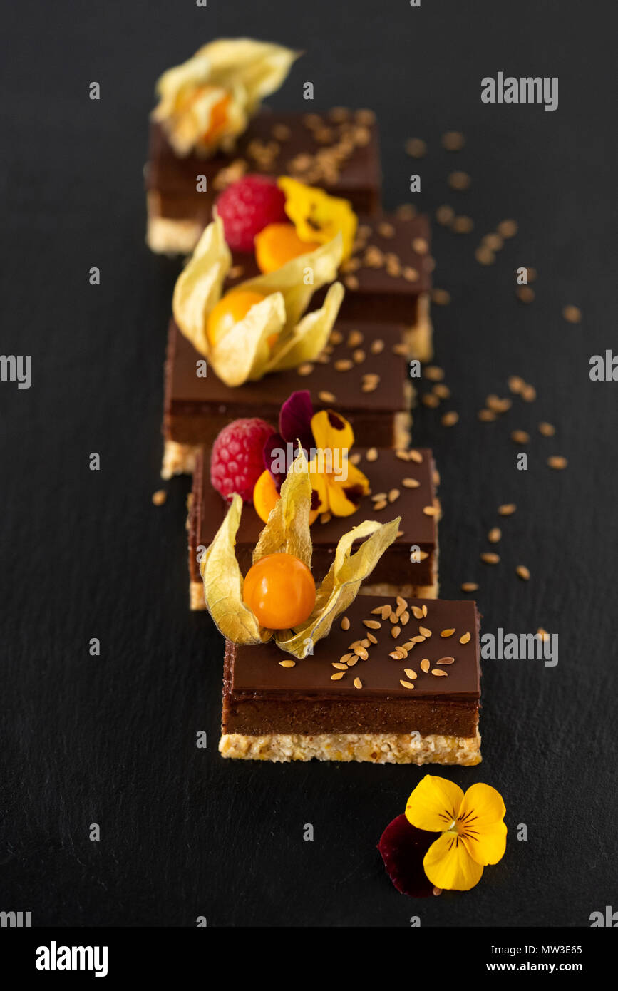 Raw vegan Schokoladenkuchen mit Physalis, Himbeeren und Blumen auf schwarzem Hintergrund Stockfoto