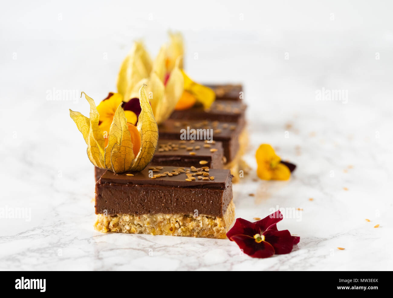Raw vegan Schokoladenkuchen mit Physalis und Blumen auf weißem Marmor Hintergrund eingerichtet Stockfoto