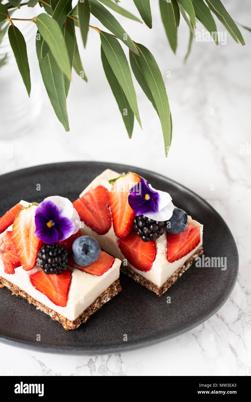 Raw vegan Mousse Cake mit Beeren und Blumen auf weißem Hintergrund Stockfoto