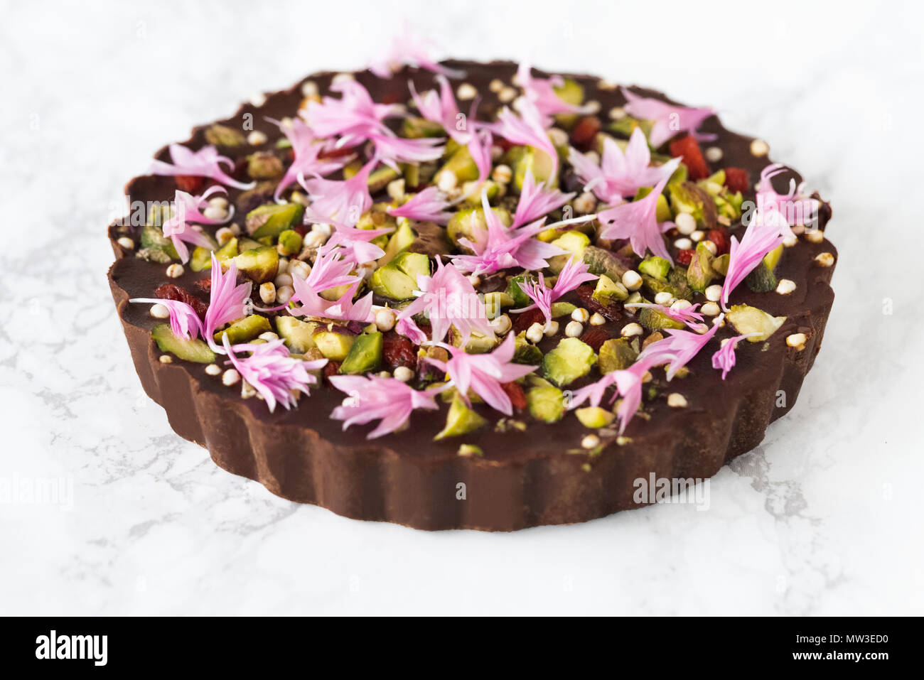 Raw vegan Schokoladentorte geschmückt mit Blumen und Pistazien auf Marmor Stockfoto