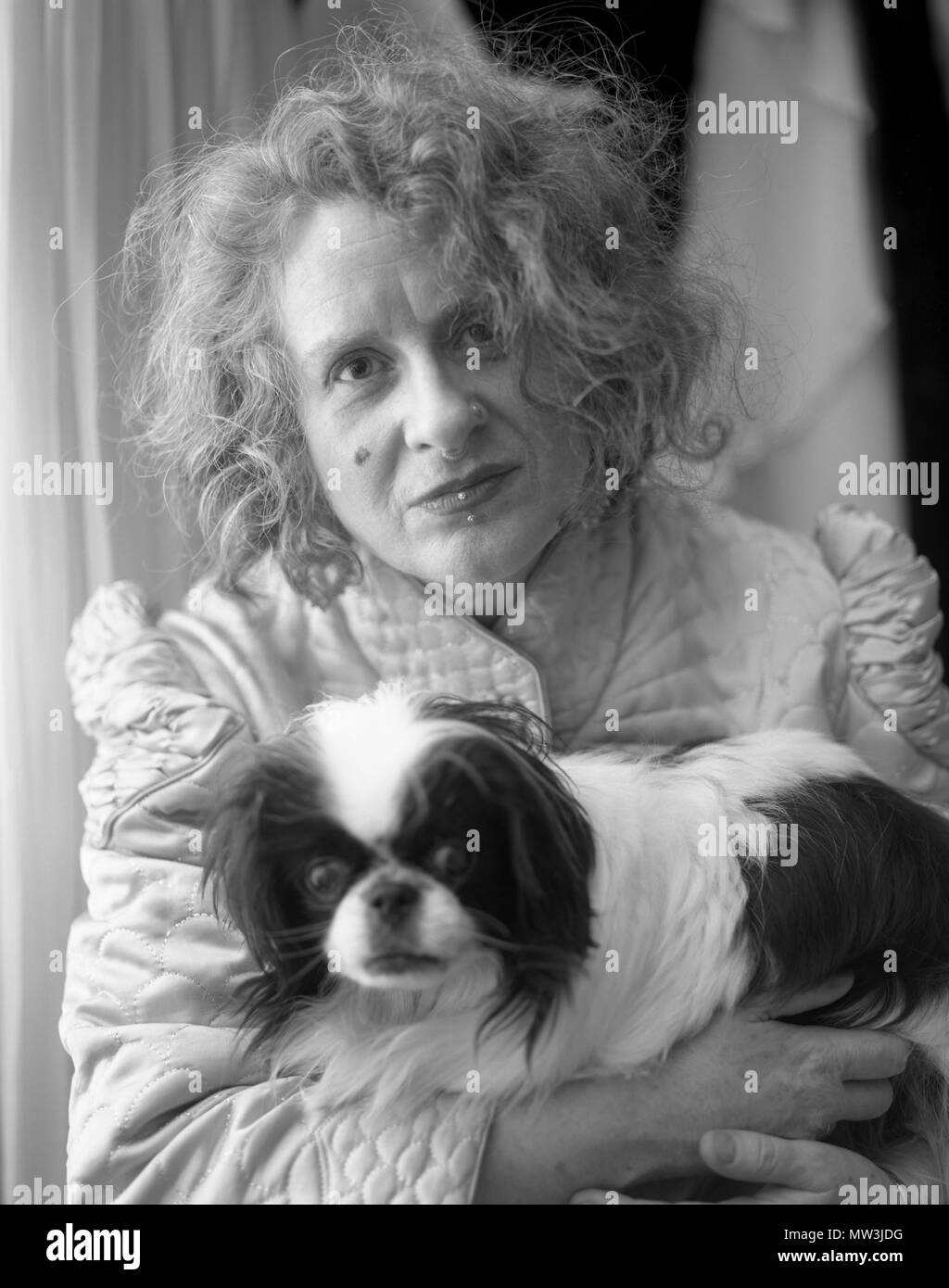 Schwarz-weiß-Porträt der Frau mit Gesichts Piercings und krauses Haar ihr Japanese Chin Rescue Dog Holding. Stockfoto