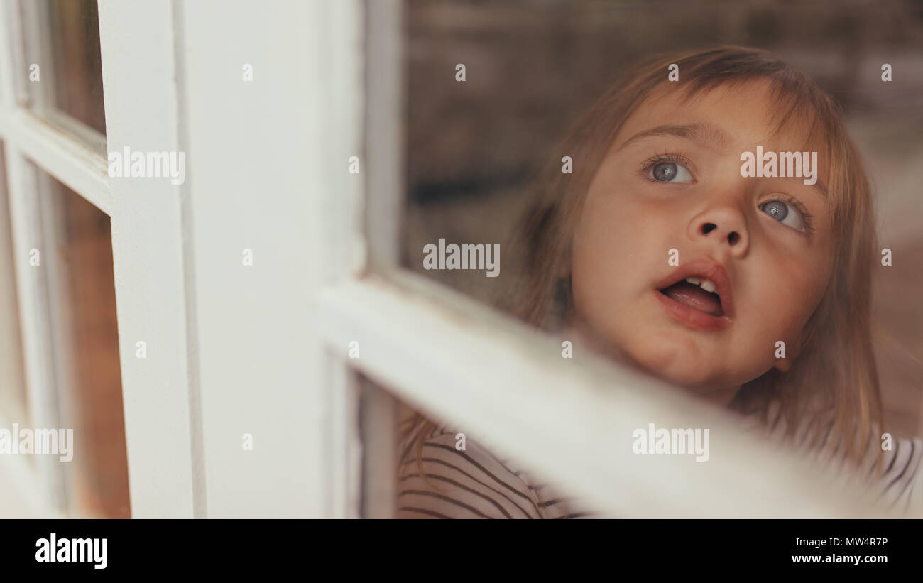 In der Nähe von einem kleinen Mädchen sitzen neben einem Fenster und Außerhalb suchen. Grau Eyed Girl suchen draußen am Fenster. Stockfoto