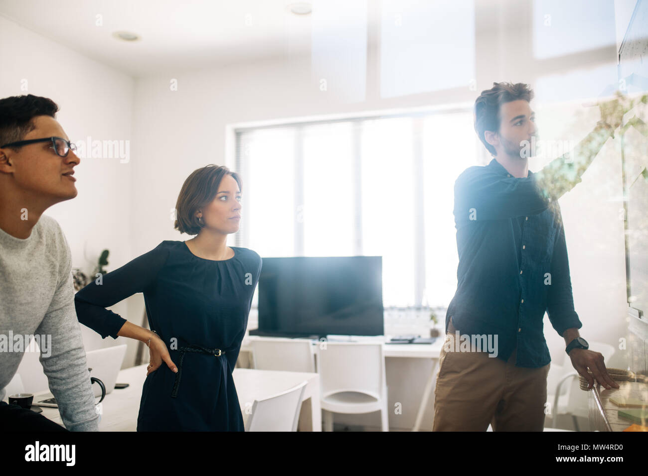 Mann schreiben an Bord im Konferenzraum, während seine Kollegen auf. Anwendungsentwickler im Diskutieren von Ideen und Arbeiten. Stockfoto
