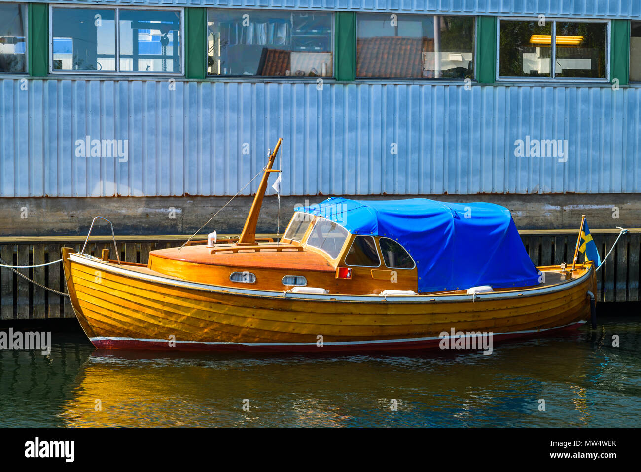 Oldtimer Holzboot mit blauer Plane, außerhalb einer industriellen Gebäude vertäut. Stockfoto