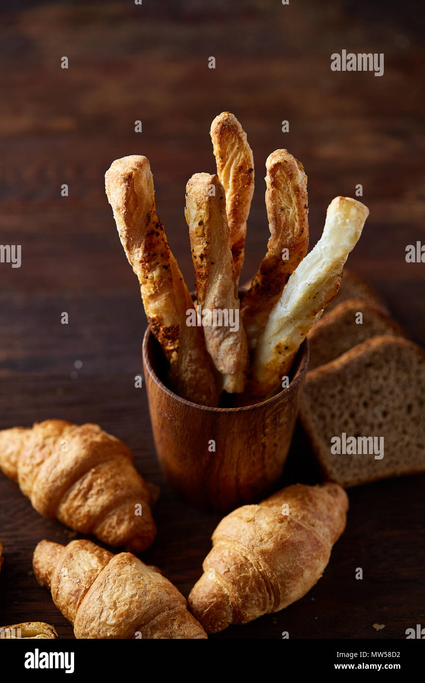 Blätterteiggebäcke auf dunklen Holztisch, Nahaufnahme, selektiver Fokus, Hintergrundbeleuchtung. Leckere frisch gebackene Grissini und hausgemachte croissats auf rustikalen backgro Stockfoto