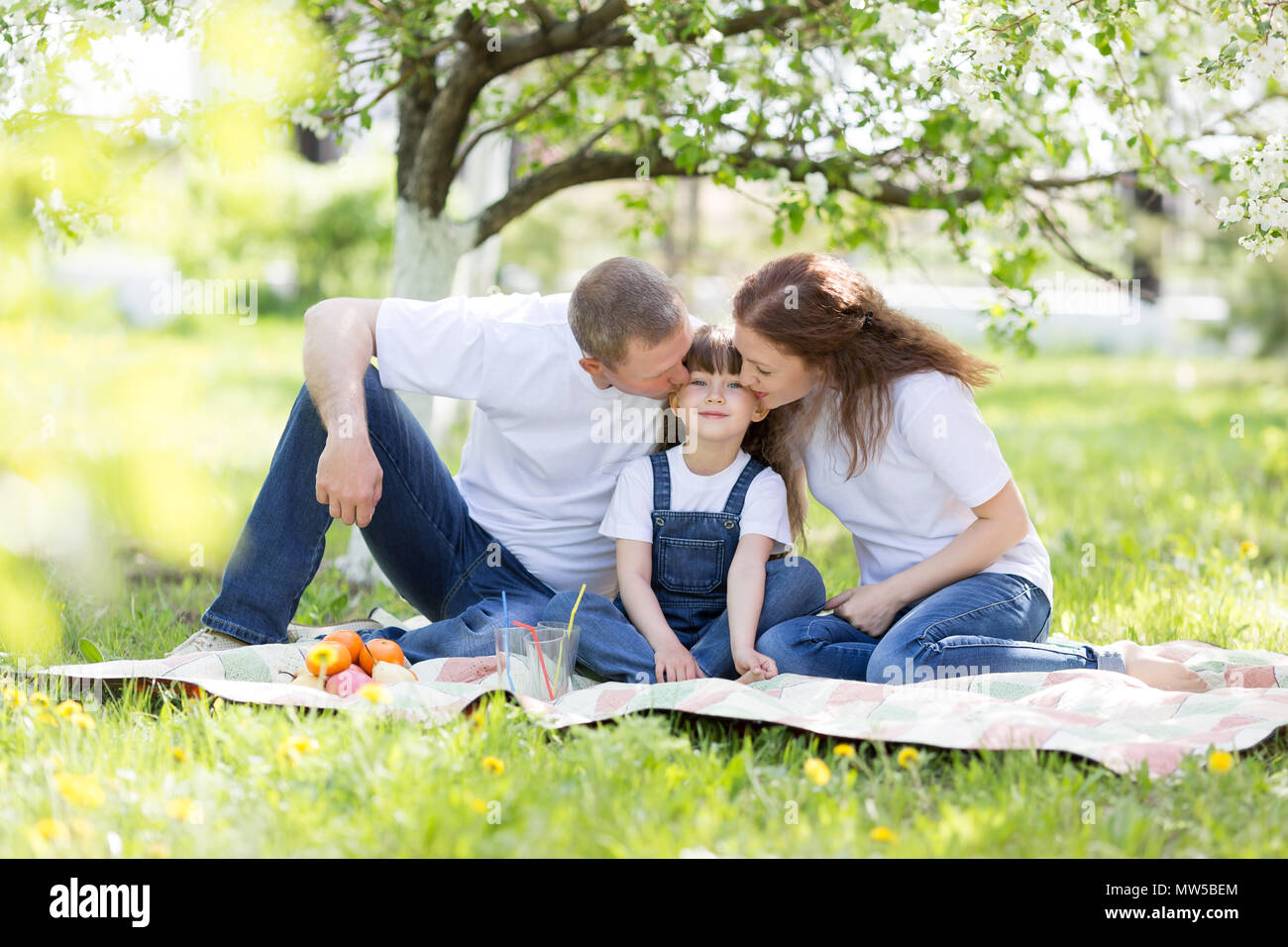 Eltern Kuss ihrer schönen Tochter sitzen unter einem Baum. Stockfoto