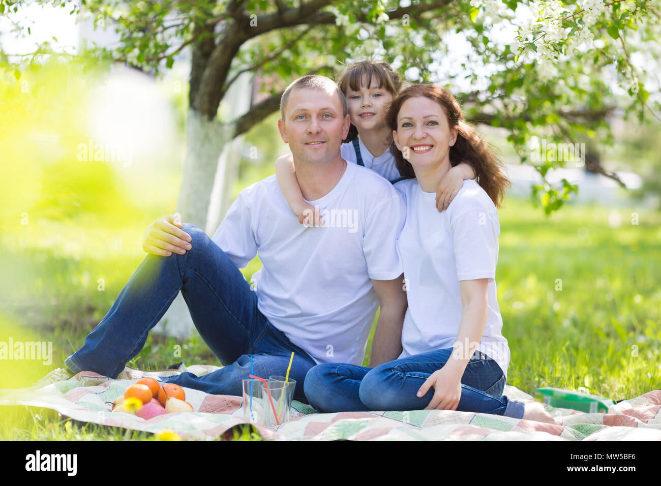 Eltern und ein 5 Jahre alten Tochter Sitzen im Garten unter einem blühenden Apfelbaum. Stockfoto