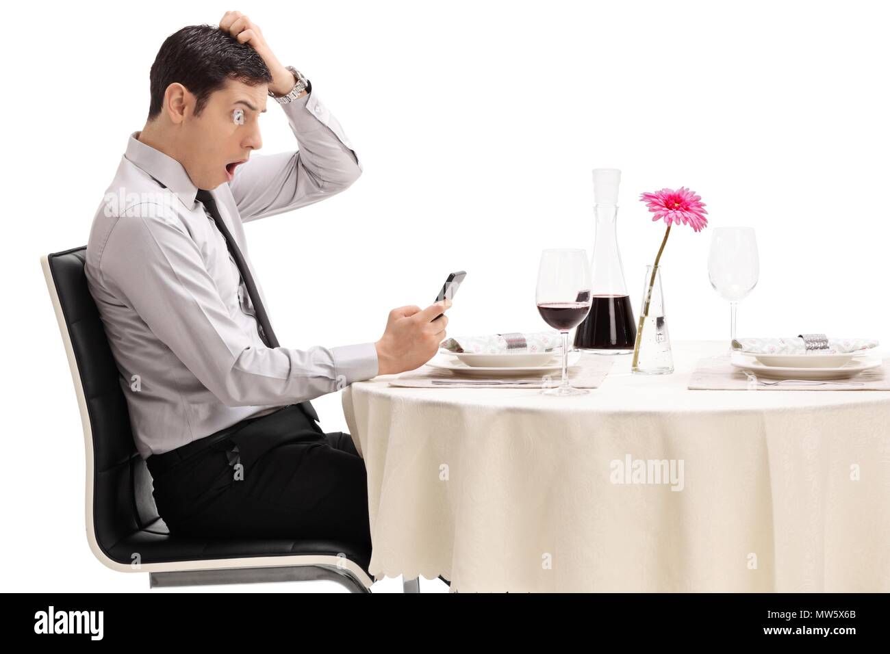 Junger Mann bei seinem Telefon an einem Tisch im Restaurant auf weißem Hintergrund sitzt Geschockt Stockfoto