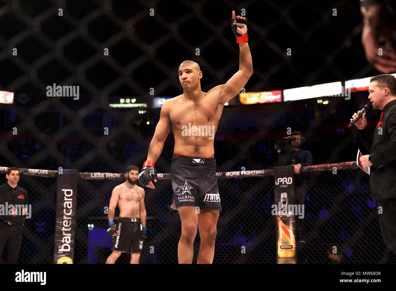 Max Nunes, Mixed Martial Artist, hebt seine Hand, während für seinen Kampf gegen Batraz Agnaev (auf dem Bild im Hintergrund) am ACB 54 Mixed Martial Arts (MMA) Veranstaltung der absoluten Meisterschaft Berkut in Manchester, UK eingeführt wird. Stockfoto