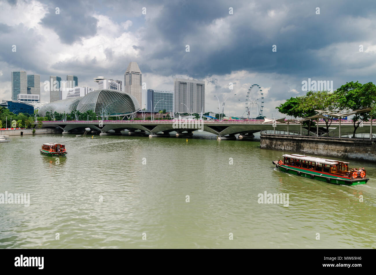 Eine Kreuzfahrt Boot wie die twakows Fahrt durch die berühmten Singapore River bekannt. Das Gebäude an der Rückseite ist die berüchtigte Theater an der Bucht, Esplanade. Stockfoto