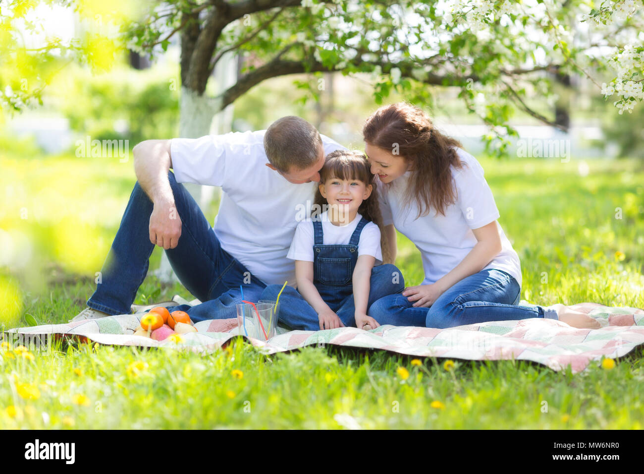 Eltern und ein 5 Jahre alten Tochter Sitzen im Garten unter einem blühenden Apfelbaum. Stockfoto