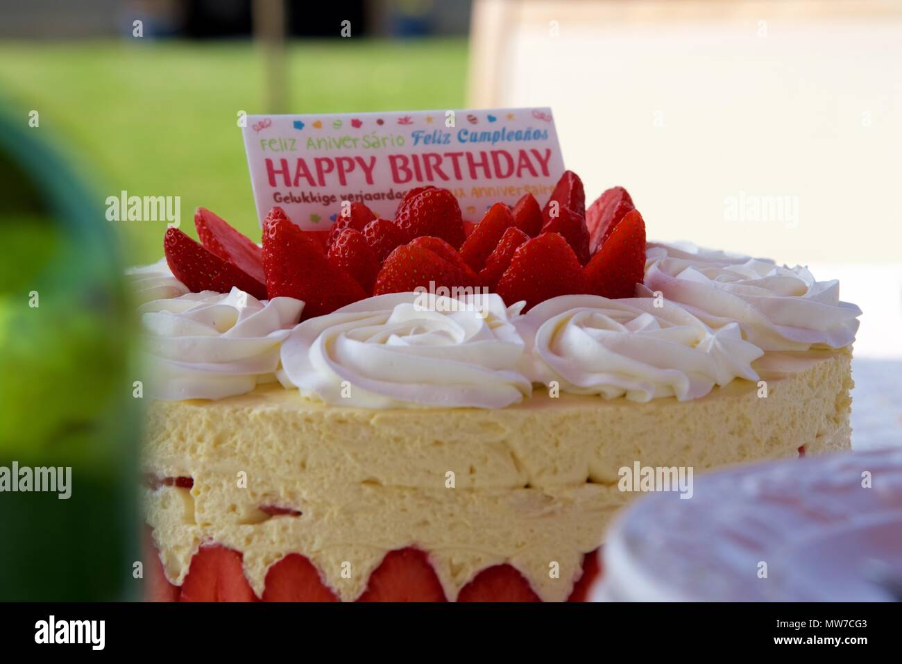 Geburtstag Kuchen: eine Erdbeere Geburtstag Kuchen mit einem mehrsprachigen Karte sagt 'Happy Birthday' Stockfoto