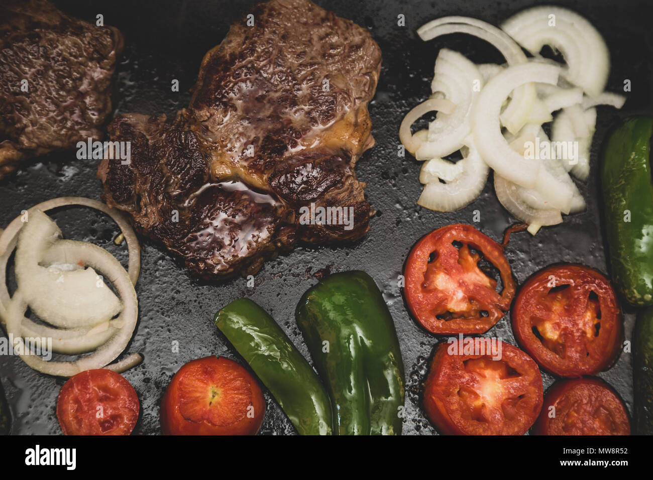 Rib Eye Steak (spanisch: Bife Ancho), Zwiebeln, Tomaten und grüne Paprika auf rechteckigem Gusseisen flache Pfanne gegrillt, vintage getönten, flach legen Stockfoto